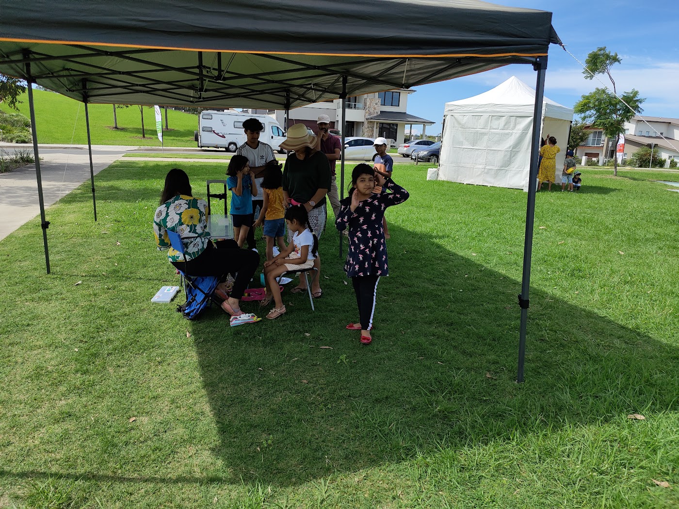 Families sitting under a marquee at a community barbecue